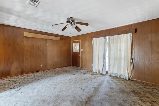 an empty room with chandelier fan and windows