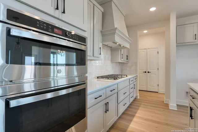 a kitchen with stainless steel appliances granite countertop a refrigerator a sink dishwasher a stove and white countertops with wooden floor