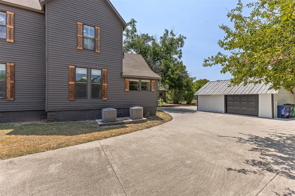 1005 North Trinity Street Decatur, TX 76234 - Photo 35 of 39 Dark gray exterior siding with decorative wood shutters, concrete driveway, and a white detached garage with a gray metal roof and dark gray garage doors