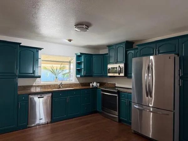 an empty room with wooden floor kitchen view and a ceiling fan