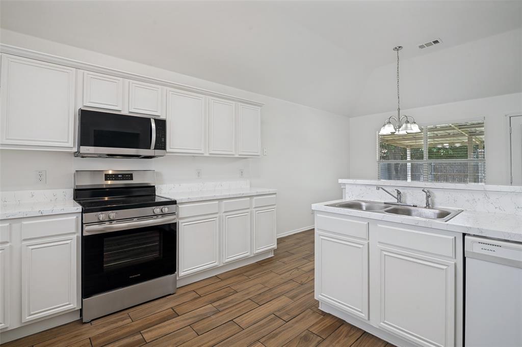 3111 Creekside Drive Sachse, TX 75048 - Photo 9 of 25 Kitchen featuring white cabinetry, wood-finish flooring, stainless steel appliances, a dual basin sink, and a breakfast bar