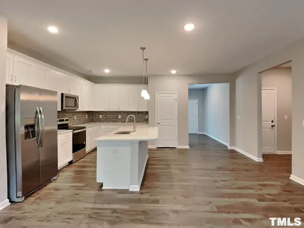 a large kitchen with kitchen island a sink dishwasher a refrigerator and white cabinets with wooden floor