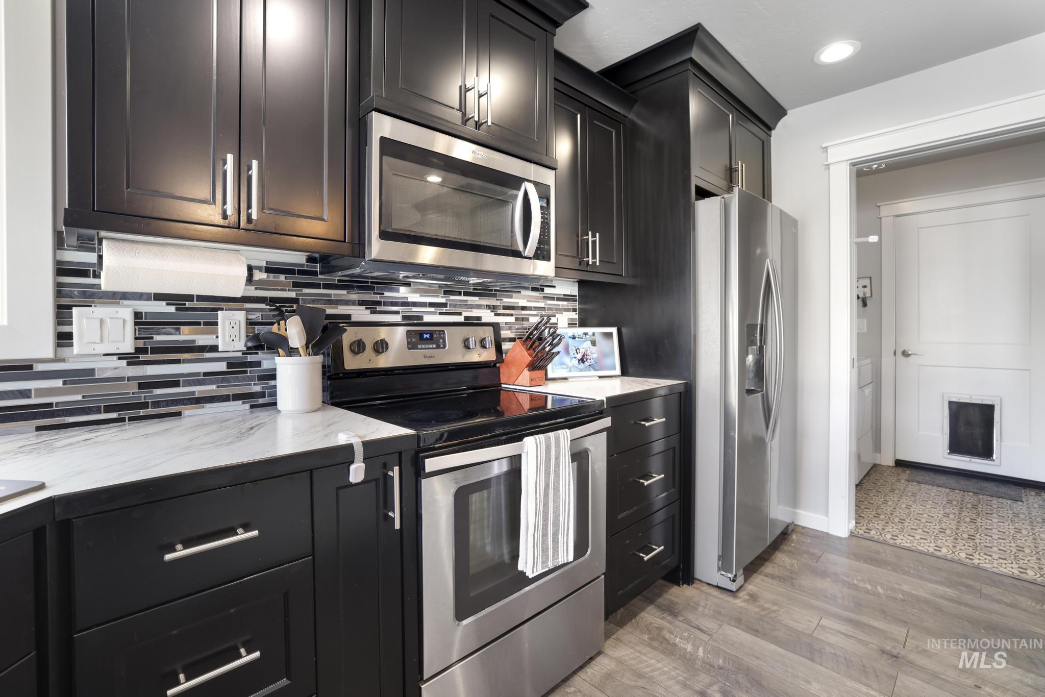 2396 Village Street Twin Falls, ID 83301 - Photo 21 of 44 Kitchen with appliances with stainless steel finishes, dark cabinets, light stone countertops, dark wood-style floors, and backsplash