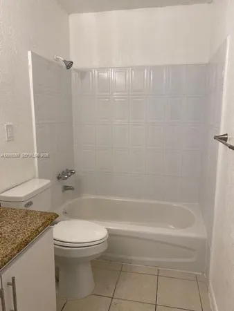 a bathroom with a granite countertop bathtub shower sink vanity and toilet