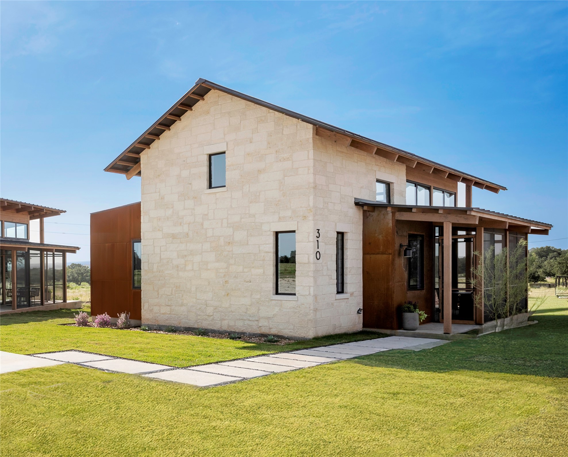 310 Hye Springs Road, Unit 107 Hye, TX 78635 - Photo 3 of 20 Modern Hill Country exterior with limestone facade, standing seam roof, and patina metal finished accents creating a refined contemporary ranch aesthetic.