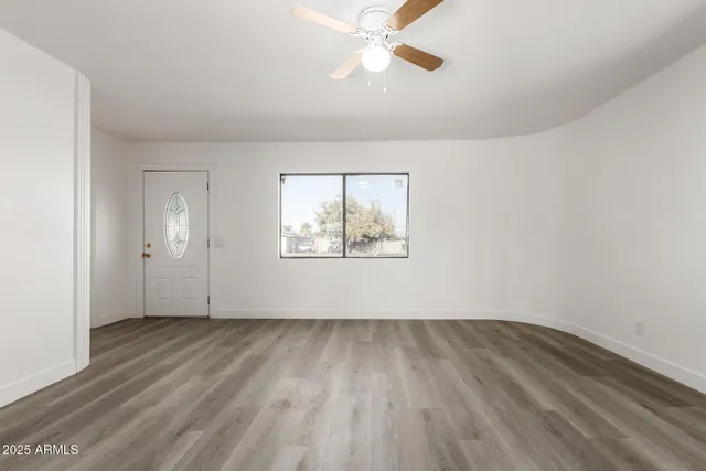 an empty room with wooden floor chandelier fan and windows