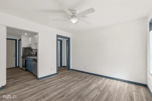 a view of an empty room with wooden floor and a ceiling fan