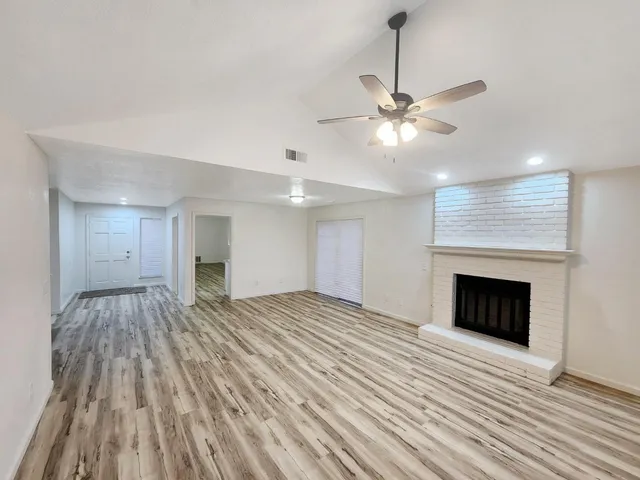 a view of an empty room with wooden floor fireplace and a window