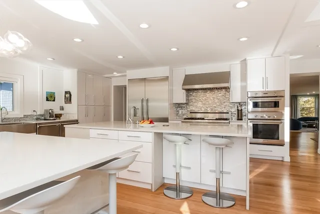 a kitchen with stainless steel appliances kitchen island granite countertop a stove a sink a refrigerator and white cabinets with wooden floor