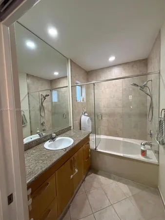 a bathroom with a granite countertop sink a mirror a bathtub and shower