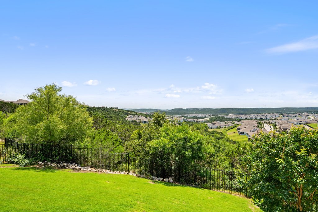 1221 Siena Sunset Road Leander, TX 78641 - Photo 35 of 39 Expansive green lawn extending to a black metal fence, overlooking a valley with distant residential development and abundant mature trees