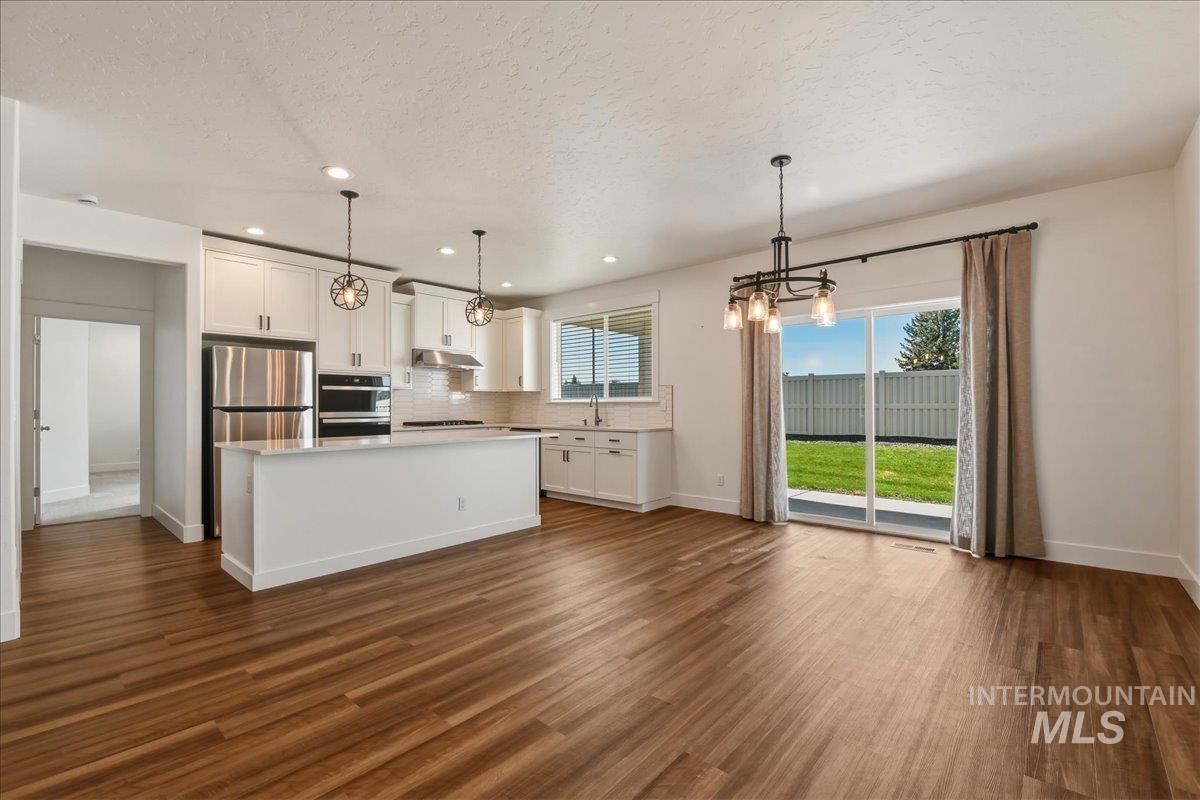 2109 North Gelding Court Middleton, ID 83644 - Photo 13 of 39 Kitchen with a kitchen island, white cabinets, suspended lighting, decorative backsplash, and dark wood-type flooring