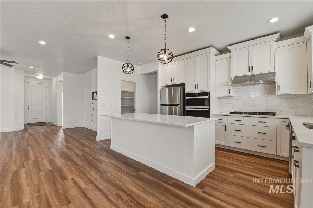 2109 North Gelding Court Middleton, ID 83644 - Photo 15 of 39 Kitchen with white cabinets, stainless steel appliances, decorative backsplash, a kitchen island, and decorative light fixtures