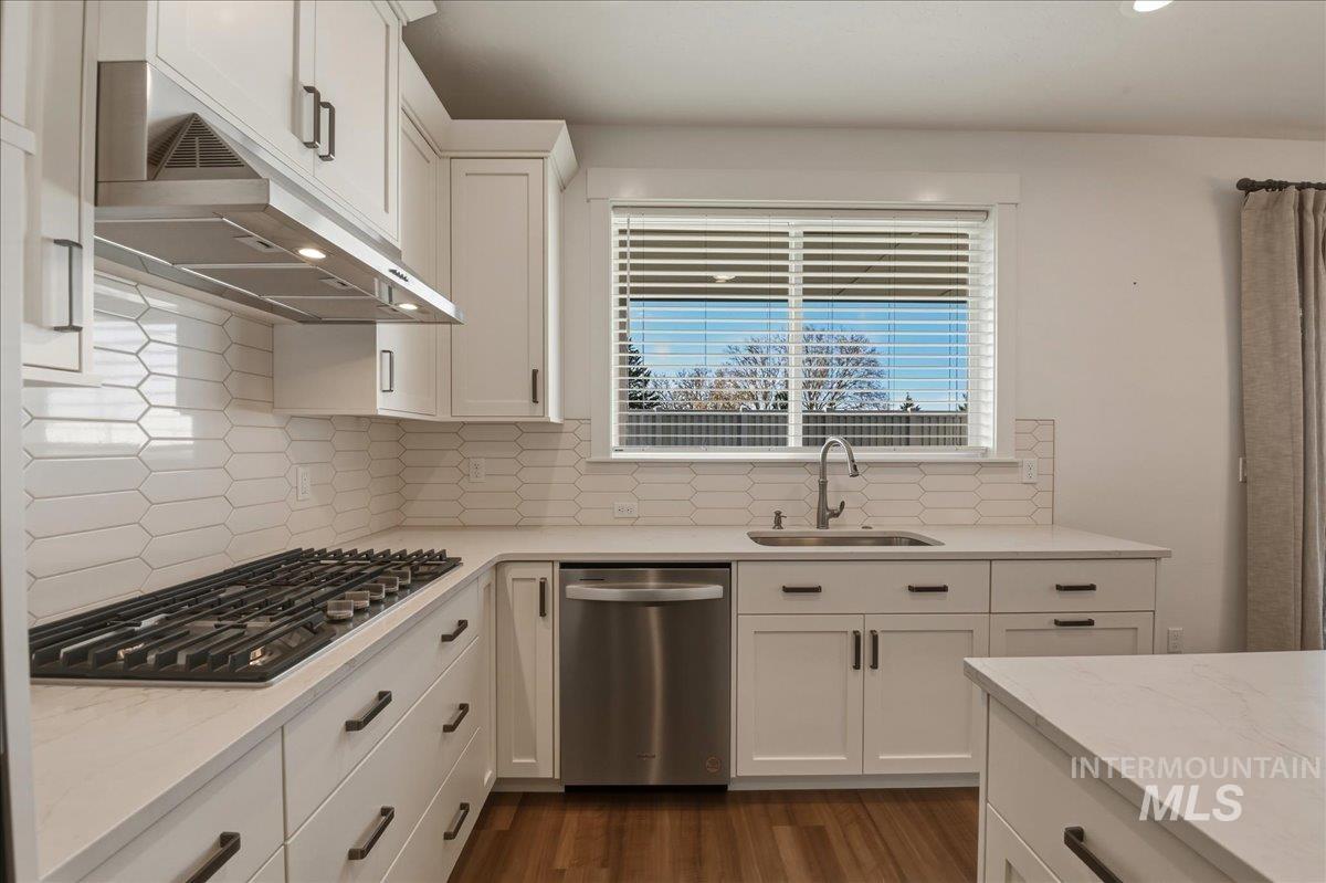 2109 North Gelding Court Middleton, ID 83644 - Photo 17 of 39 Kitchen featuring white cabinets, stainless steel appliances, dark wood-style floors, light stone counters, and backsplash