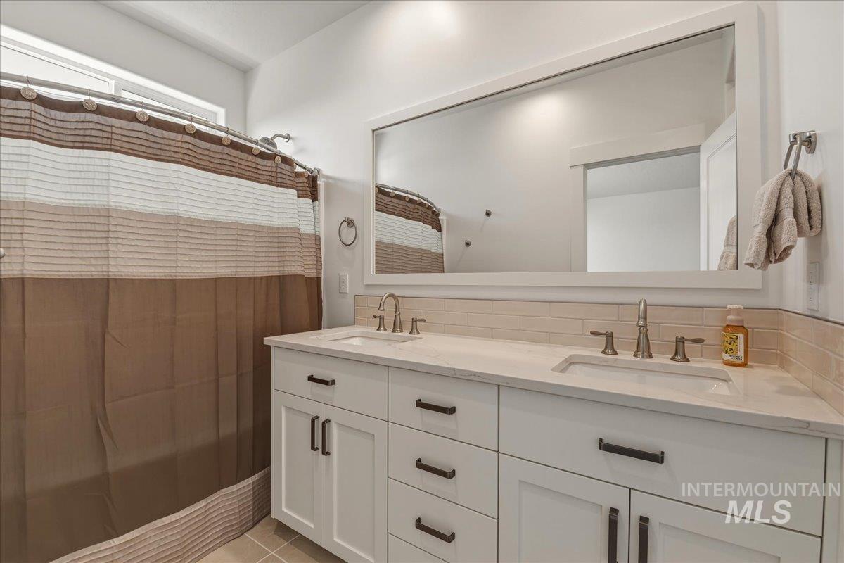 2109 North Gelding Court Middleton, ID 83644 - Photo 22 of 39 Bathroom featuring double vanity, curtained shower, backsplash, and light tile patterned floors