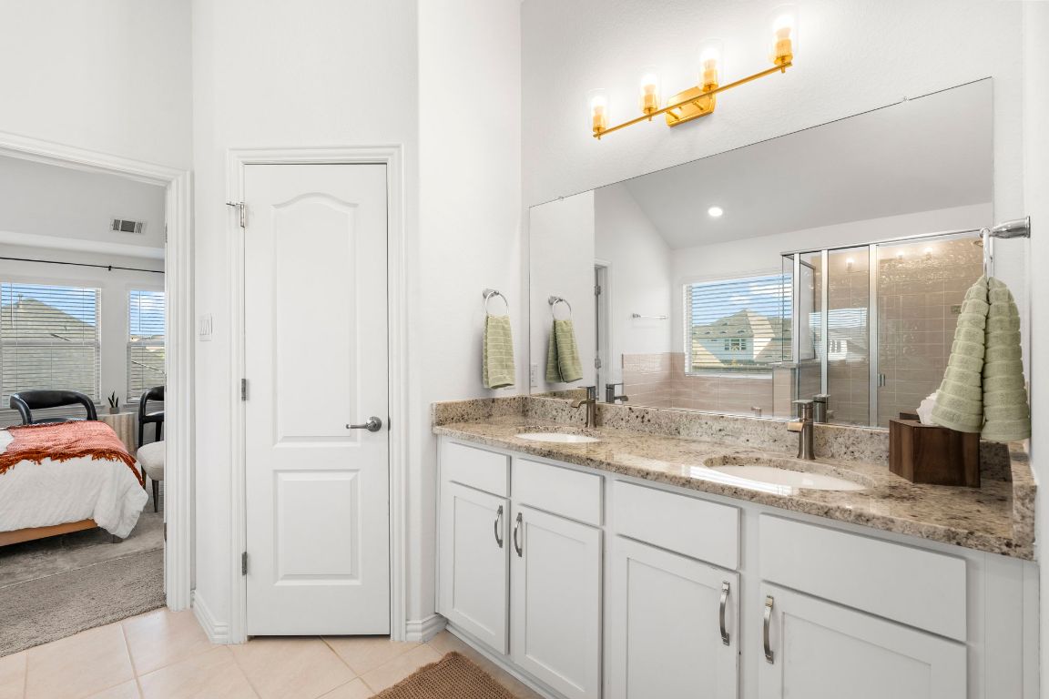 463 Oleander Loop Buda, TX 78610 - Photo 16 of 34 Full bathroom with double vanity, a stall shower, connected bathroom, tile patterned floors, and lofted ceiling