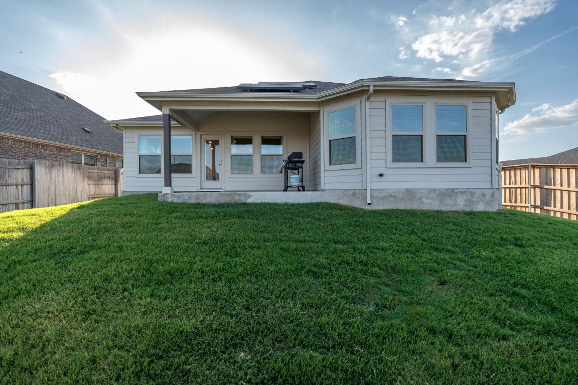 463 Oleander Loop Buda, TX 78610 - Photo 17 of 34 Back of house with solar panels, a fenced backyard, and a patio