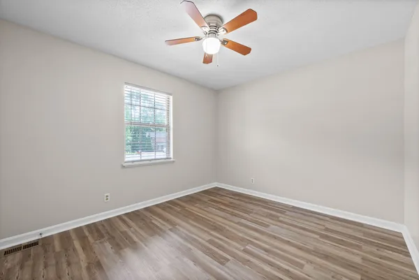 an empty room with wooden floor fan and windows