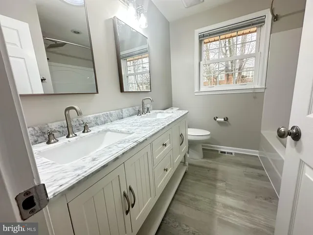 a spacious bathroom with a double vanity sink toilet mirror and a window