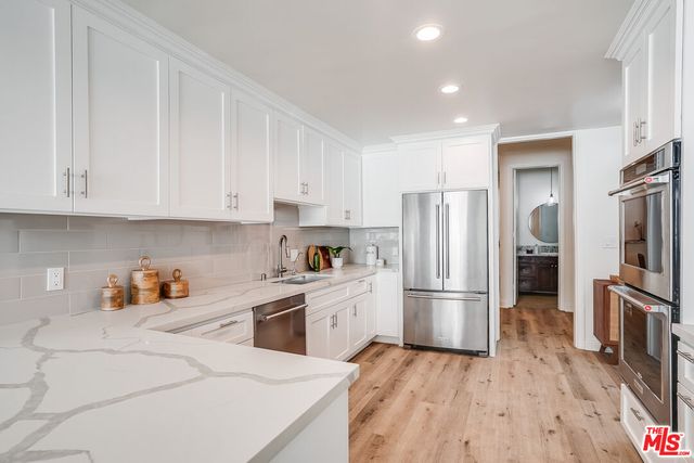 a kitchen with stainless steel appliances granite countertop a refrigerator oven a sink dishwasher and white cabinets with wooden floor