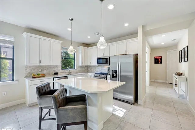 a kitchen with stainless steel appliances kitchen island granite countertop a refrigerator a stove a sink a dining table and chairs with white cabinets