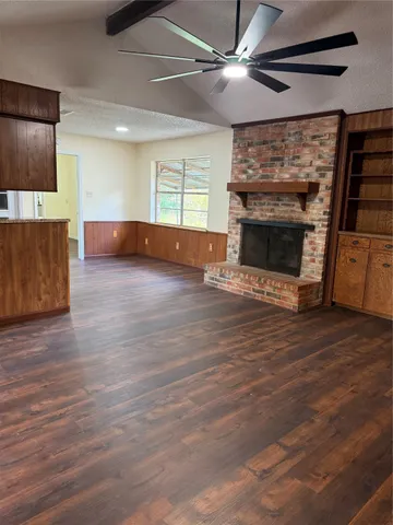 a view of an empty room with wooden floor fireplace and a window