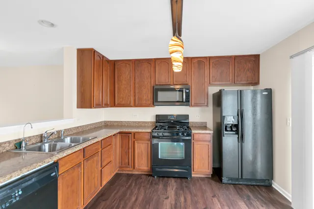 a kitchen with stainless steel appliances granite countertop a refrigerator a sink dishwasher and wooden cabinets with wooden floor