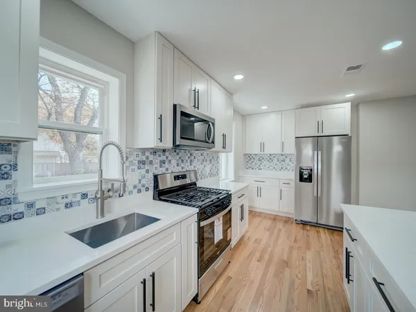 a kitchen with white cabinets a sink a stove a refrigerator and a stove with wooden floor