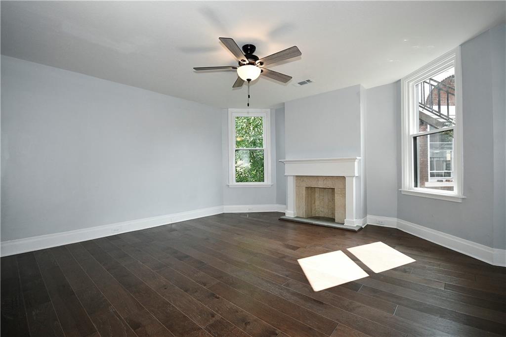 6029 Stanton Avenue Pittsburgh, PA 15206 - Photo 13 of 27 an empty room with wooden floor a fireplace a ceiling fan and windows