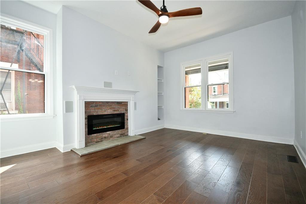 6029 Stanton Avenue Pittsburgh, PA 15206 - Photo 6 of 27 an empty room with wooden floor a fireplace and windows