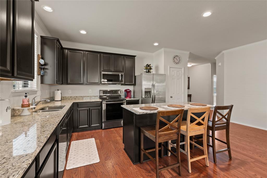 537 Running Water Trail Fort Worth, TX 76131 - Photo 11 of 31 a kitchen with stainless steel appliances kitchen island granite countertop a sink a stove a kitchen island with chairs and wooden floor