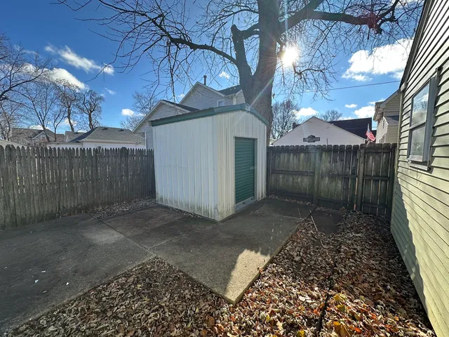 a view of a white house with a large tree and wooden fence