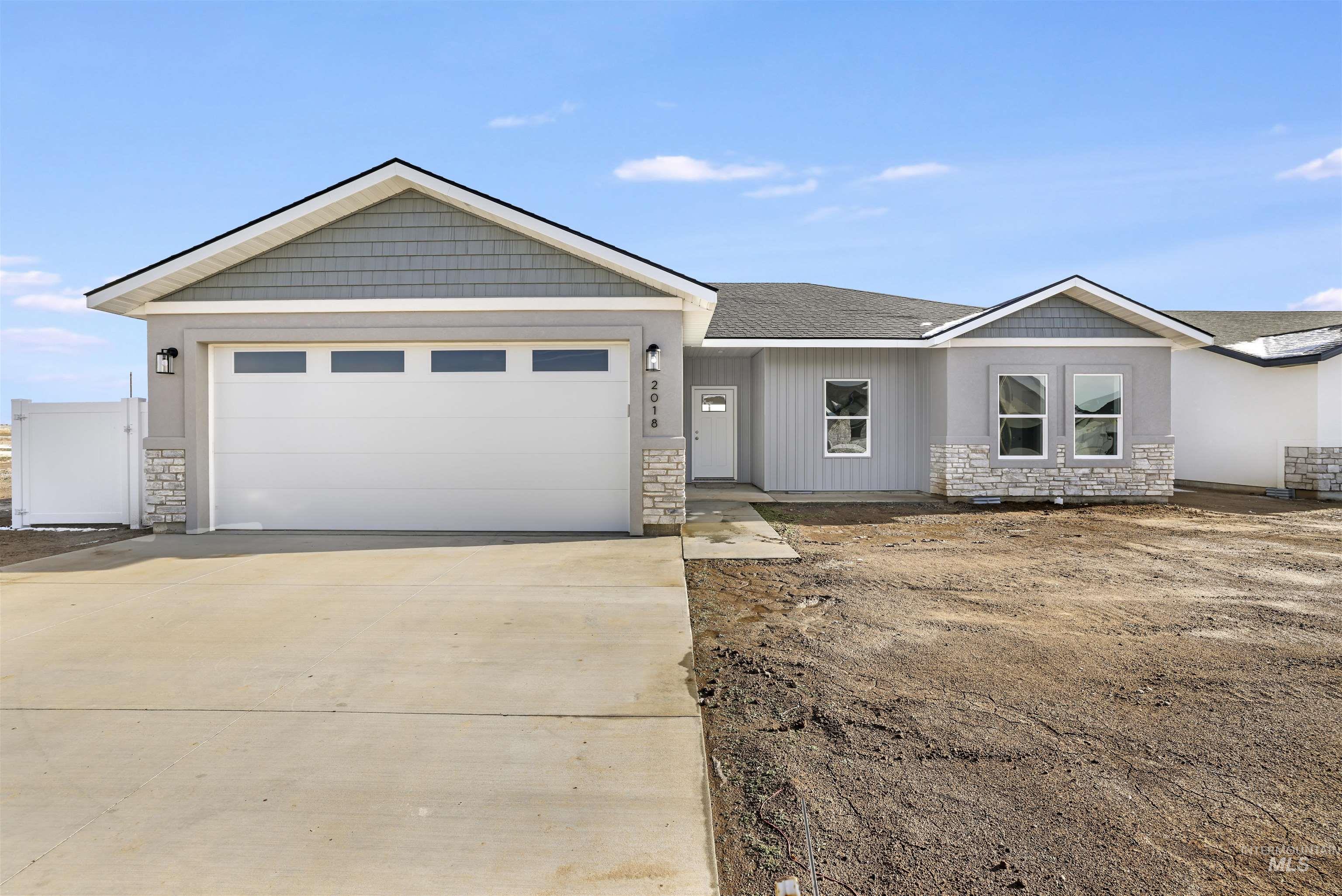 View of front facade with stone siding, driveway, an attached garage, and roof with shingles