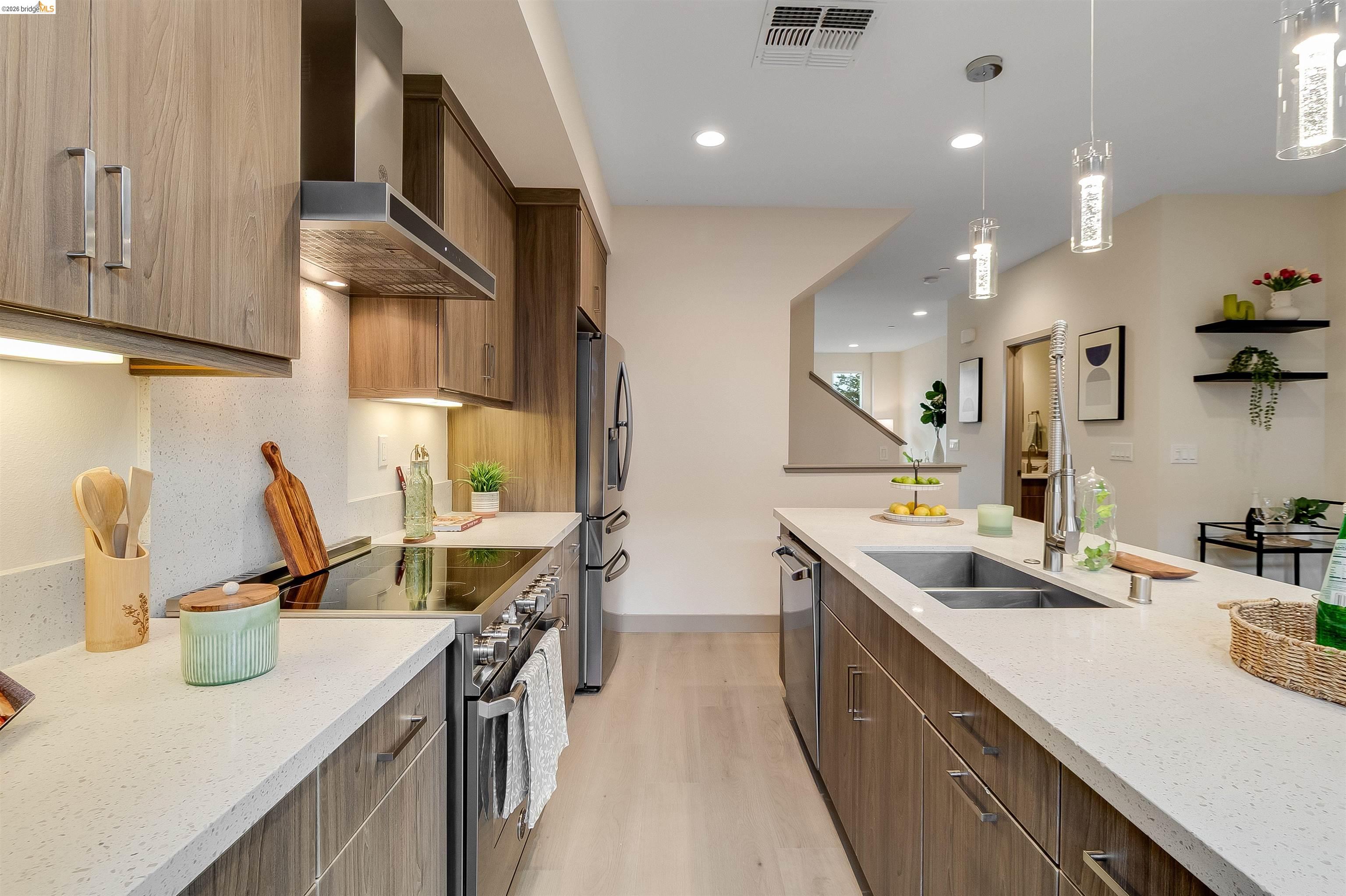 1357 Pullman Way Oakland, CA 94607 - Photo 11 of 37 Modern kitchen featuring wood-finish cabinetry, light-toned countertops, stainless steel appliances, and a central island with an undermount sink