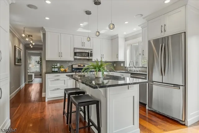 a kitchen with stainless steel appliances granite countertop a refrigerator a stove a sink a dining table and chairs with wooden floor