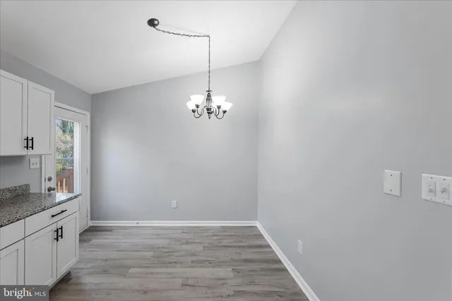 a view of an empty room with wooden floor and a kitchen