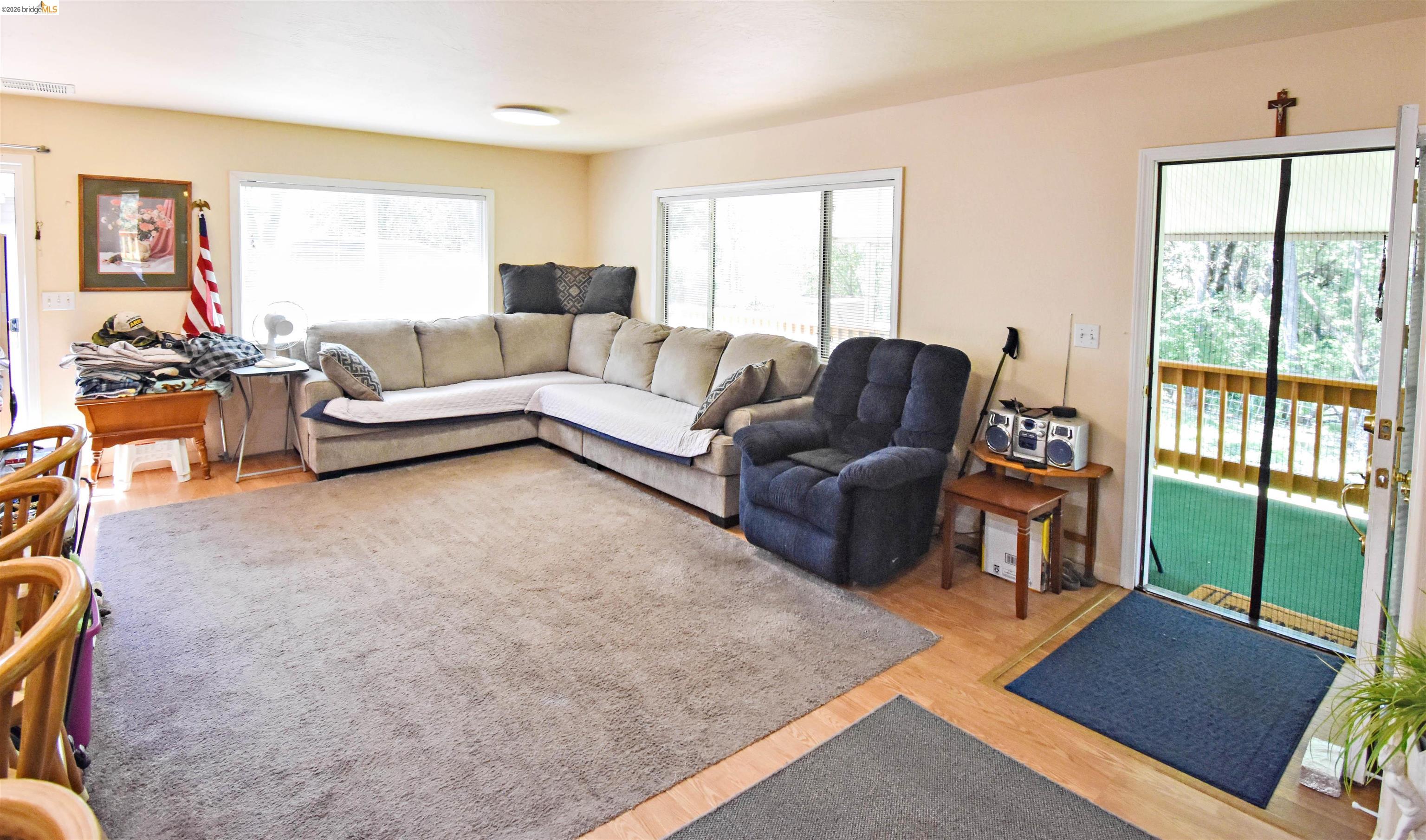 13904 Tuolumne Road Sonora, CA 95370 - Photo 17 of 44 Living area featuring light wood-finish flooring, a large area rug, multiple windows, and a door opening to a balcony with wood railings