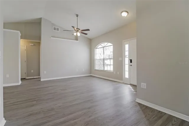an empty room with wooden floor ceiling fan and windows