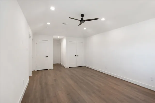 an empty room with wooden floor a ceiling fan and kitchen view
