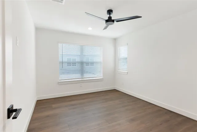 an empty room with wooden floor ceiling fan and windows