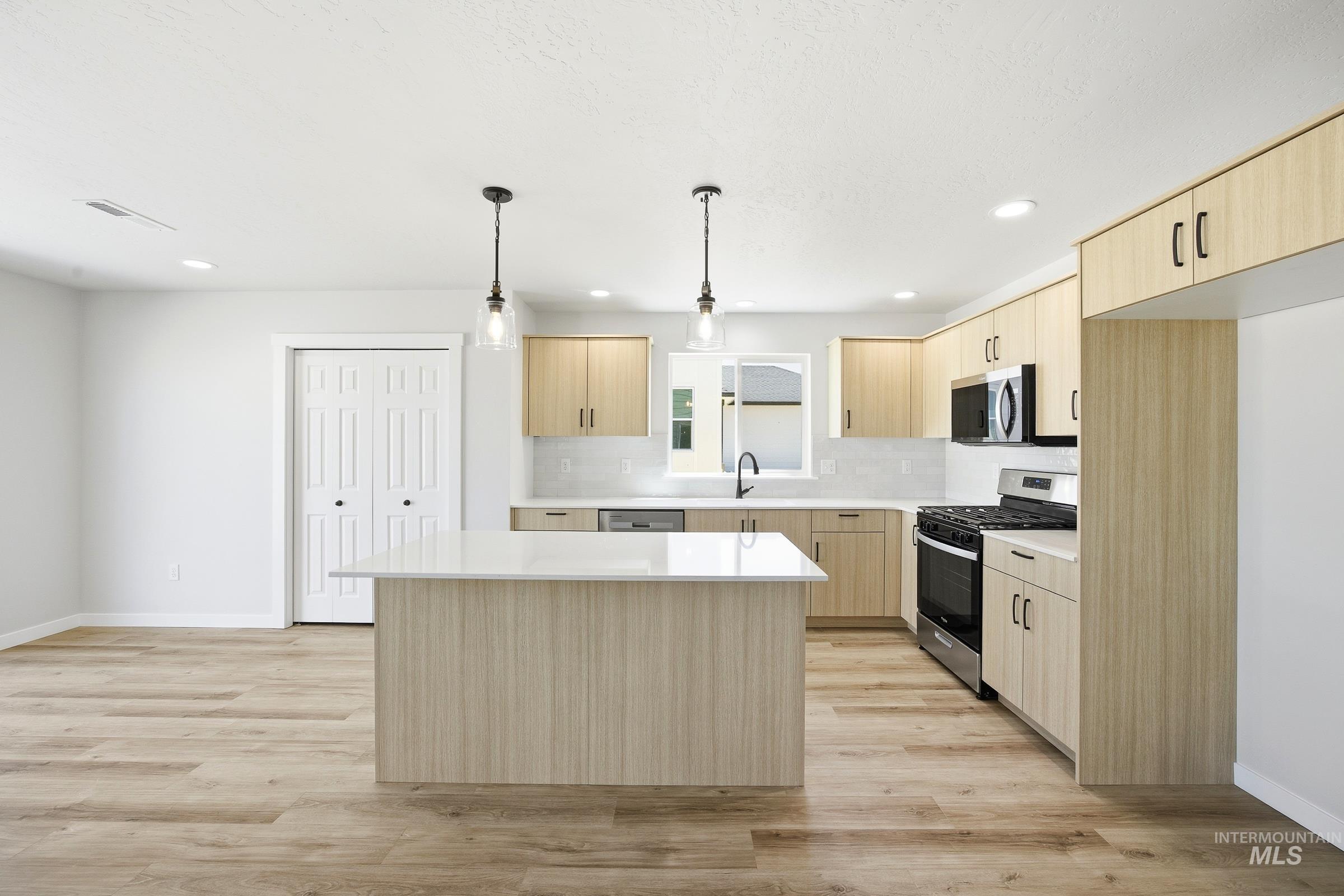 12841 Decatur Street Nampa, ID 83651 - Photo 3 of 30 Kitchen features a central island with a white countertop, light wood-finish cabinetry, stainless steel appliances, and a white subway tile backsplash