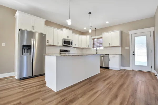a kitchen with stainless steel appliances granite countertop a refrigerator a stove top oven a sink dishwasher and a refrigerator with wooden floor