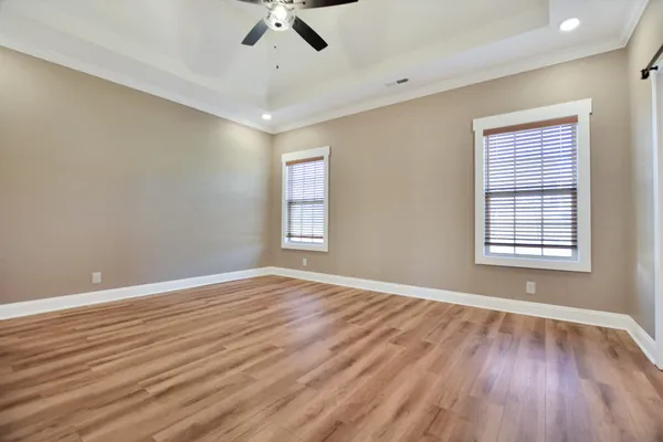 an empty room with wooden floor fan and windows