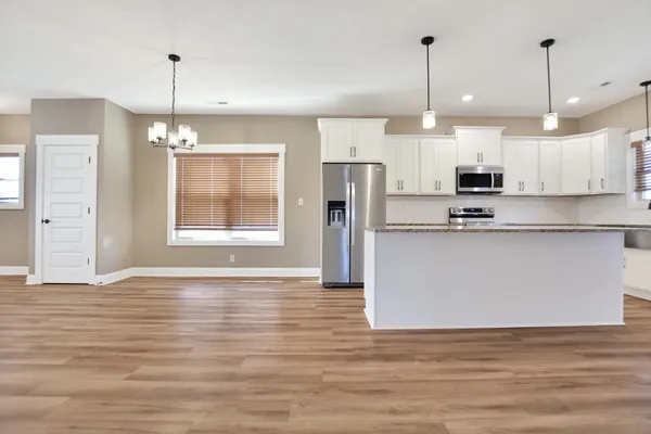 a kitchen with stainless steel appliances granite countertop a refrigerator a sink dishwasher a stove and white cabinets with wooden floor