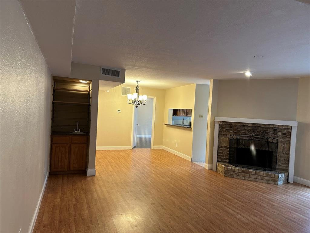 336 Melrose Drive, Unit 7B Richardson, TX 75080 - Photo 7 of 18 Unfurnished living room featuring wood finished floors, a chandelier, and a fireplace with raised hearth