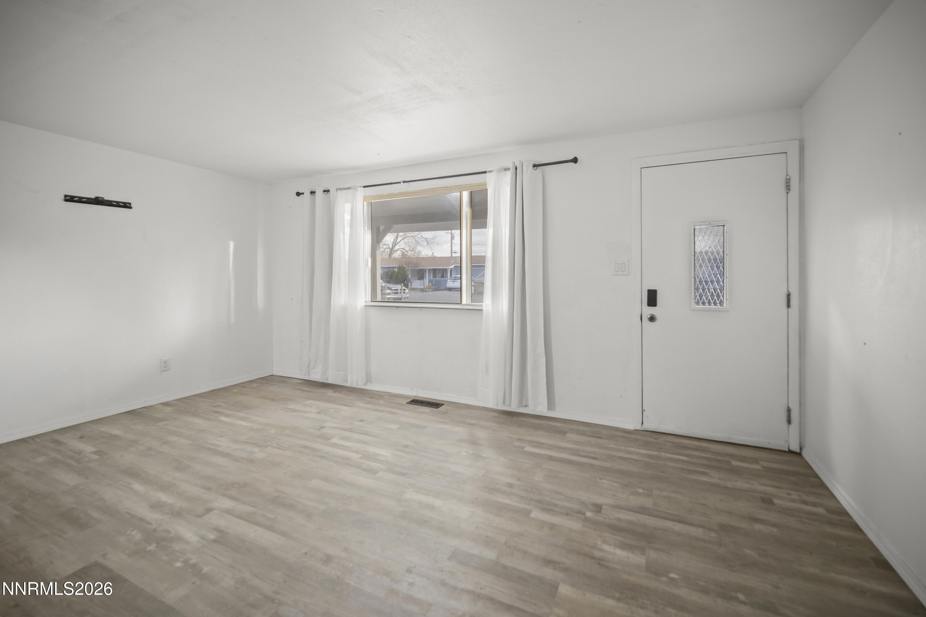150 McCart Street Fernley, NV 89408 - Photo 4 of 28 a view of an empty room with wooden floor and a window