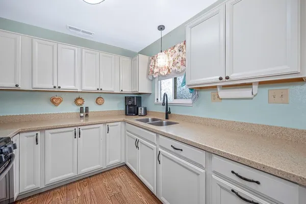 a kitchen with a sink dishwasher and white cabinets with wooden floor