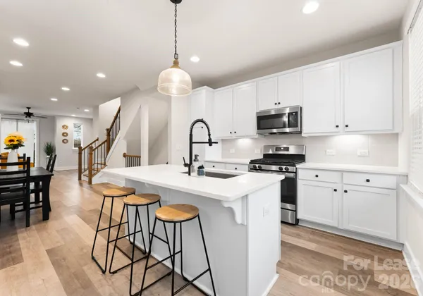 a kitchen with stainless steel appliances kitchen island granite countertop a sink a stove a dining table and chairs with wooden floor