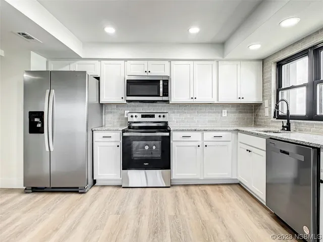 a kitchen with stainless steel appliances granite countertop a refrigerator stove a sink and white cabinets