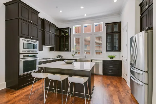 a kitchen with stainless steel appliances kitchen island granite countertop a refrigerator a stove and a sink with wooden floor